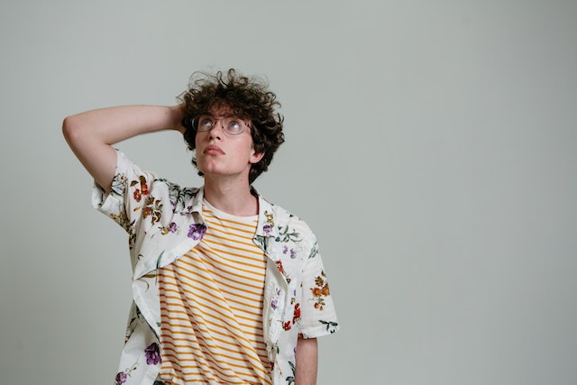 Jongen met hawaishirt kijkt naar boven en gaat met hand door krullend haar